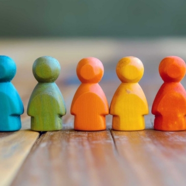 A row of wooden colorful figures against a blurred indoor background, symbolizing unity in diversity